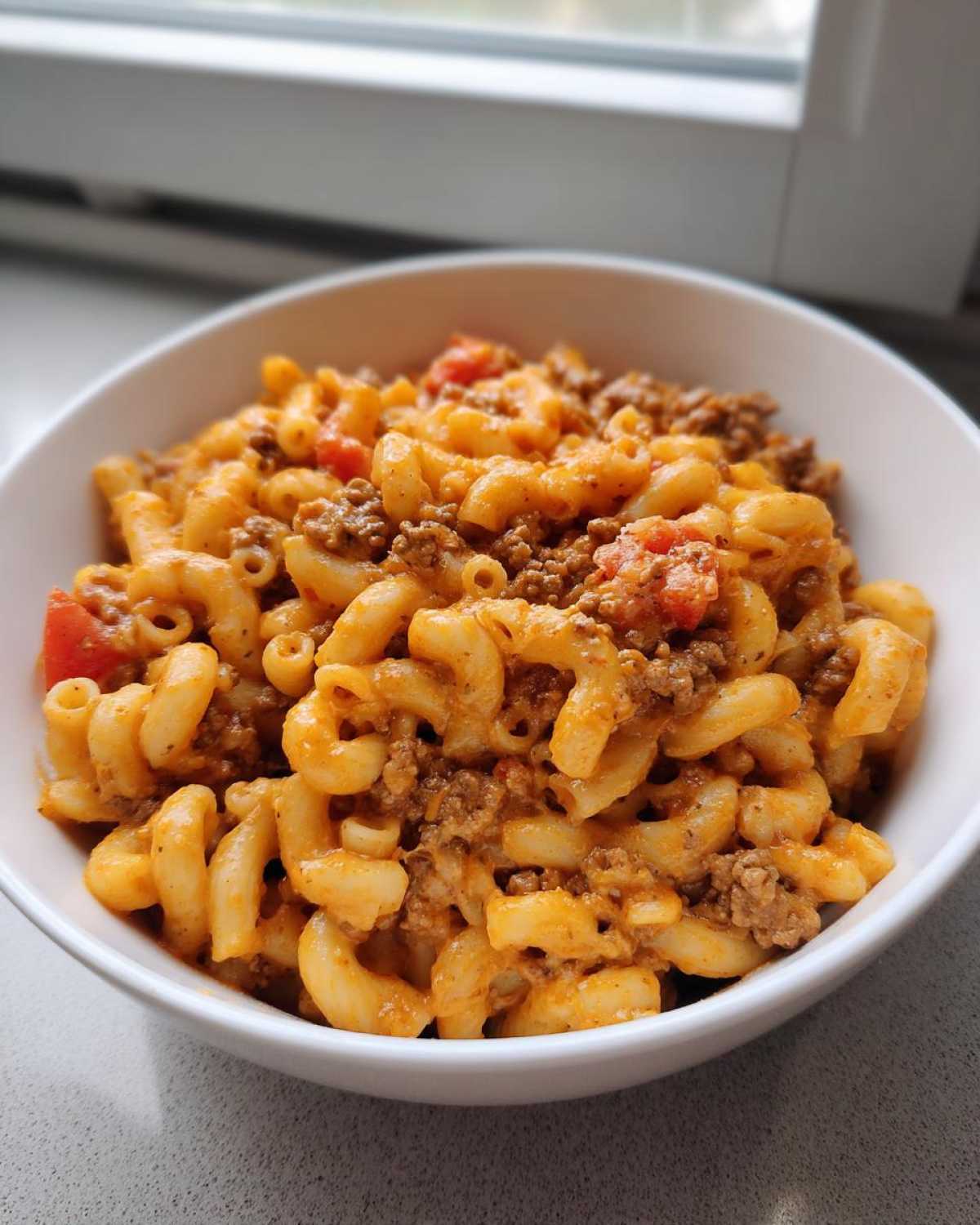A close-up shot of a white bowl filled with creamy One Pot Taco Pasta mixed with ground beef and diced tomatoes.