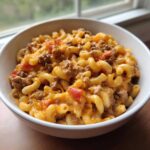 A close-up of creamy, cheesy One Pot Taco Pasta with ground beef and tomatoes served in a white bowl.