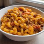 A close-up of a white bowl filled with cheesy One Pot Taco Pasta mixed with ground beef and tomatoes.
