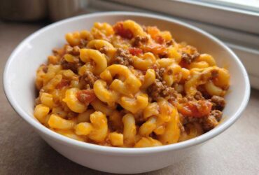 A close-up of a white bowl filled with cheesy One Pot Taco Pasta mixed with ground beef and tomatoes.