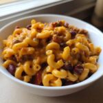A close-up view of a white bowl filled with cheesy Vegetarian Chili Mac, featuring elbow macaroni, kidney beans, and melted cheddar.