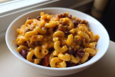 A close-up view of a white bowl filled with cheesy Vegetarian Chili Mac, featuring elbow macaroni, kidney beans, and melted cheddar.