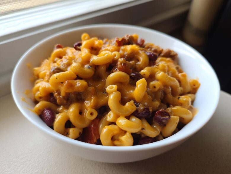 A close-up view of a white bowl filled with cheesy Vegetarian Chili Mac, featuring elbow macaroni, kidney beans, and melted cheddar.