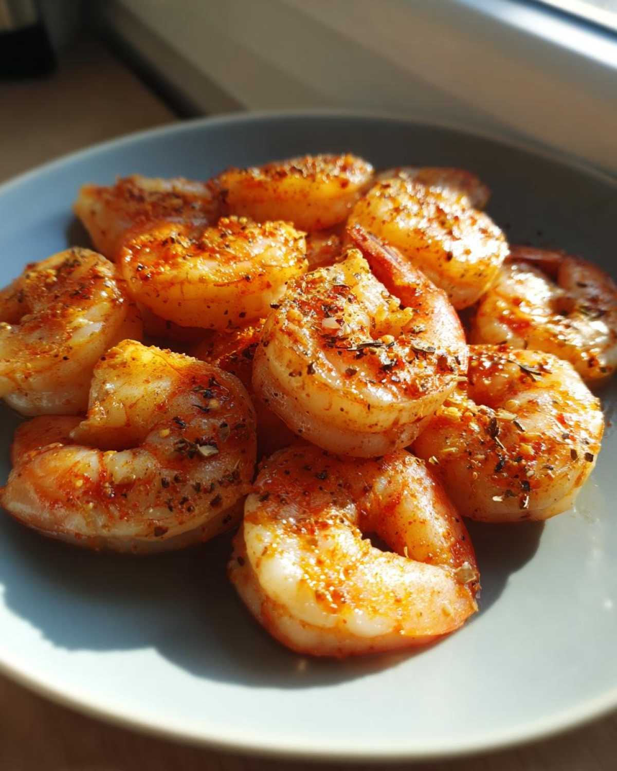 A close-up of perfectly cooked Oven Grilled Shrimp seasoned with spices, served on a light blue plate in natural light.