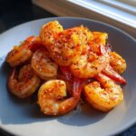 A close-up of seasoned Oven Grilled Shrimp piled high on a gray plate, glistening with spices.