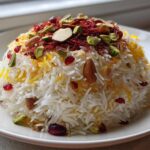 A dome of fluffy white Persian Jeweled Rice Shirin Polo topped with saffron threads, almonds, pistachios, and pomegranate seeds.