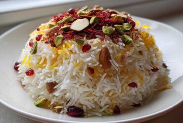 A dome of fluffy white Persian Jeweled Rice Shirin Polo topped with saffron threads, almonds, pistachios, and pomegranate seeds.