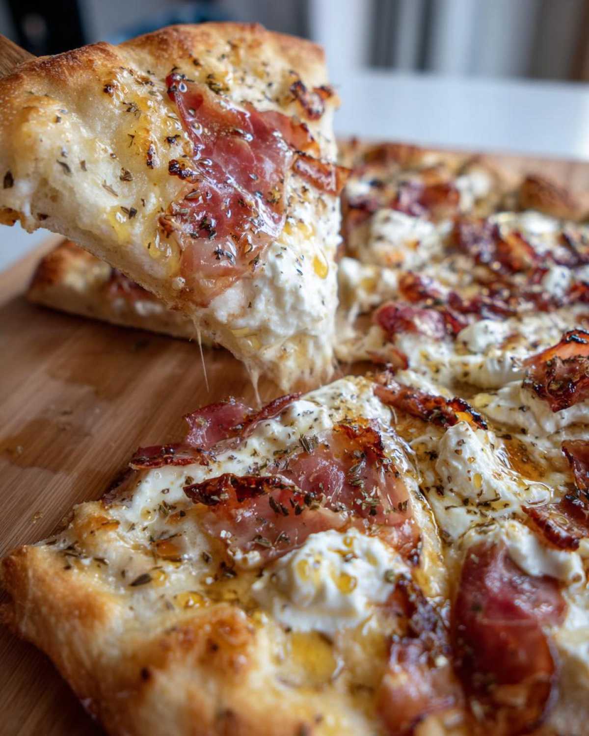 A slice of Prosciutto Honey Burrata Pizza being lifted, showing melted burrata cheese and a honey drizzle.