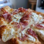 A close-up shot of a slice of Prosciutto Honey Burrata Pizza, showing melted cheese, ribbons of prosciutto, and dollops of creamy burrata.