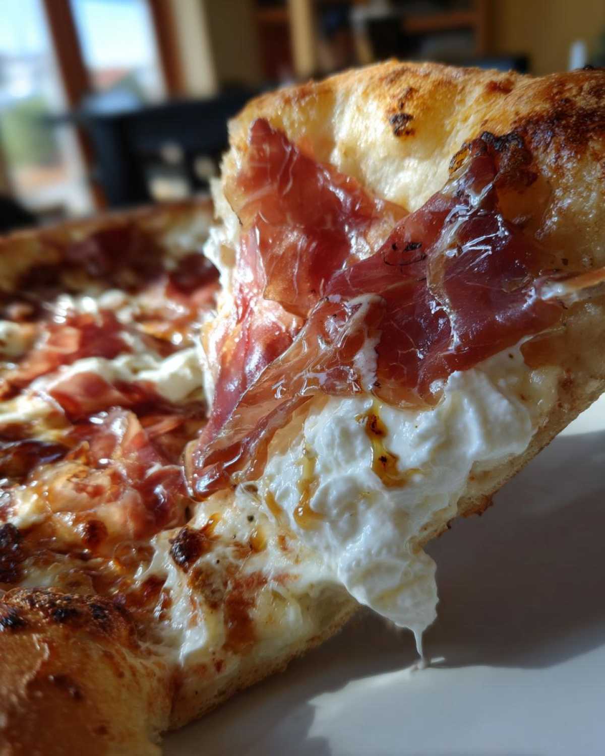 Close-up of a slice of Prosciutto Honey Burrata Pizza showing melted burrata cheese and draped prosciutto.