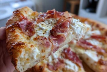 A close-up shot of a slice of Prosciutto Honey Burrata Pizza, showing melted cheese, ribbons of prosciutto, and dollops of creamy burrata.