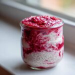A glass jar filled with layered Raspberry Chia Seed Pudding, showing white chia seeds swirled with bright red raspberry puree.