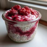 Close-up of Raspberry Chia Seed Pudding layered with creamy white base and bright red raspberry swirl, topped with fresh raspberries.