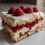 A layered slice of Raspberry Tiramisu featuring ladyfingers, cream, and bright red raspberry filling, topped with whole raspberries.