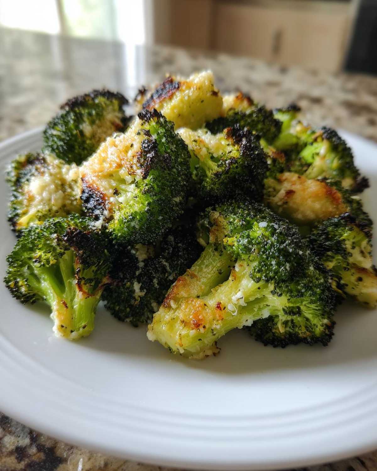 Close-up of perfectly roasted Garlic Parmesan Broccoli florets with crispy, browned edges served on a white plate.