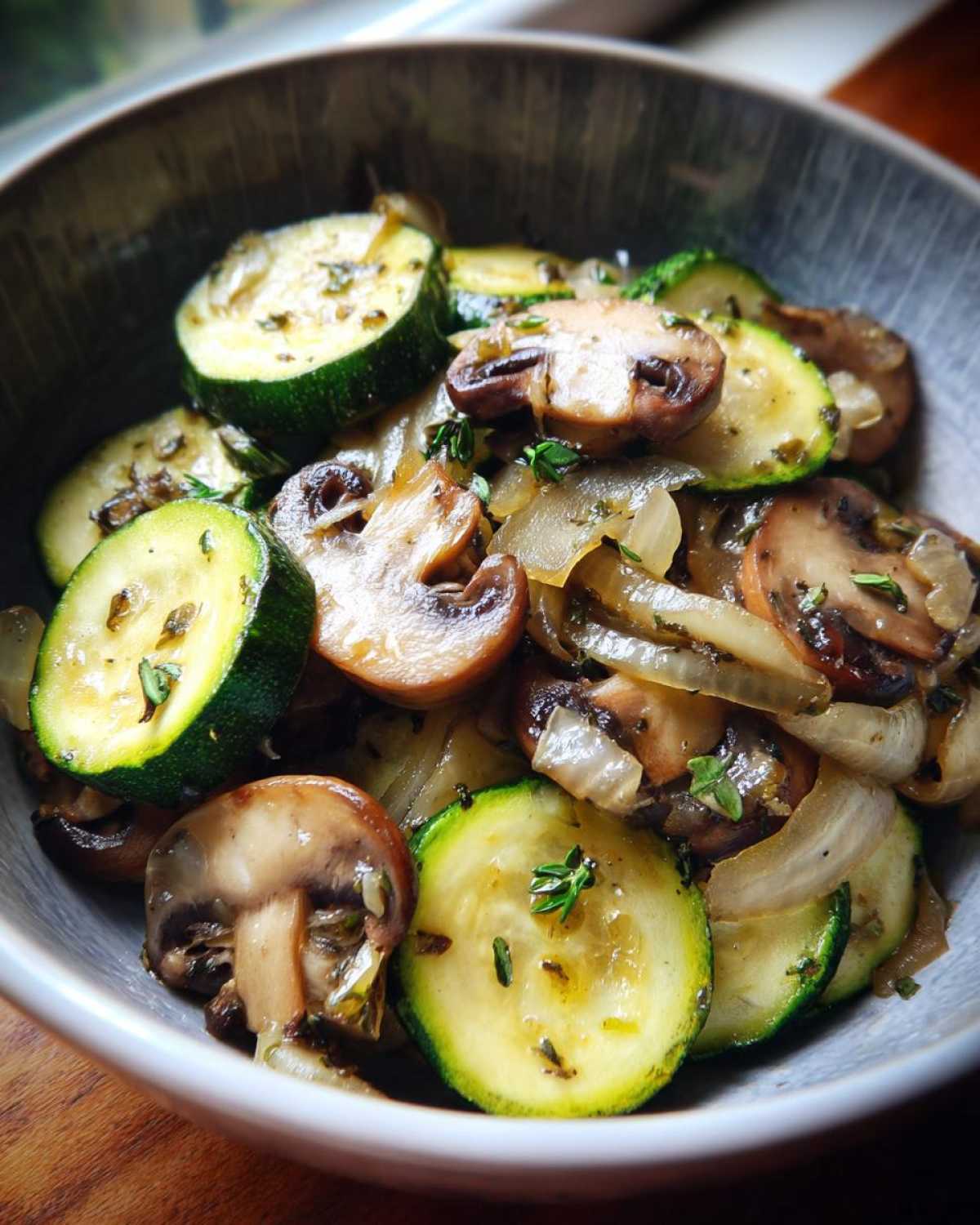 Close-up of Sauteed Zucchini Mushrooms And Onions seasoned with herbs in a rustic bowl.