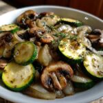 A close-up of Sauteed Zucchini Mushrooms And Onions seasoned with herbs in a white bowl.