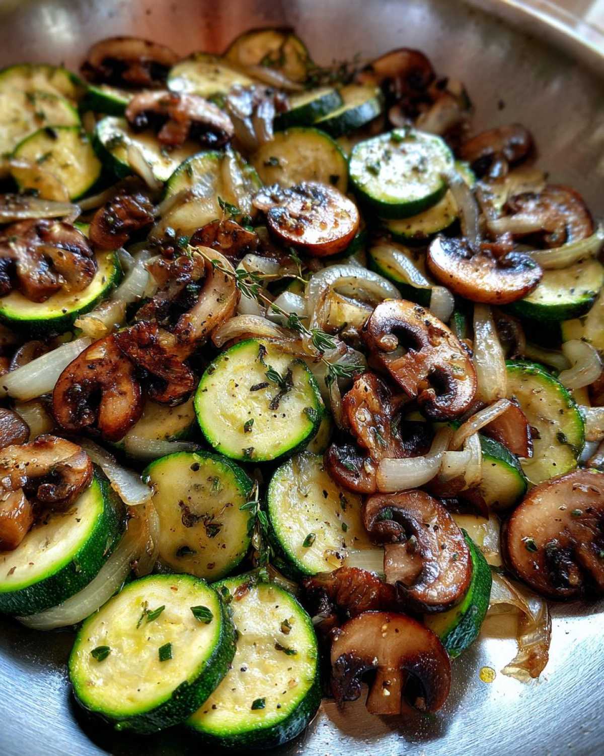 Close-up of perfectly Sauteed Zucchini Mushrooms And Onions seasoned with herbs in a metal skillet.