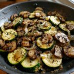 Close-up of Sauteed Zucchini Mushrooms And Onions seasoned with herbs in a dark skillet.