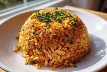 A perfectly molded mound of Savory Garlic Butter Crispy Rice, golden brown and topped with fresh chopped parsley, served on a white plate.