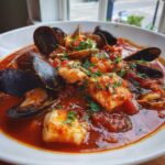 Close-up of a rich, red tomato-based Cioppino stew filled with mussels, clams, and chunks of white fish, garnished with parsley.