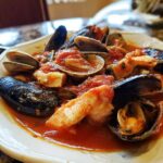 A close-up of a bowl of rich seafood Cioppino featuring mussels, clams, and shrimp in a vibrant tomato broth.