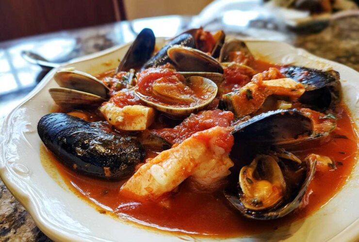 A close-up of a bowl of rich seafood Cioppino featuring mussels, clams, and shrimp in a vibrant tomato broth.