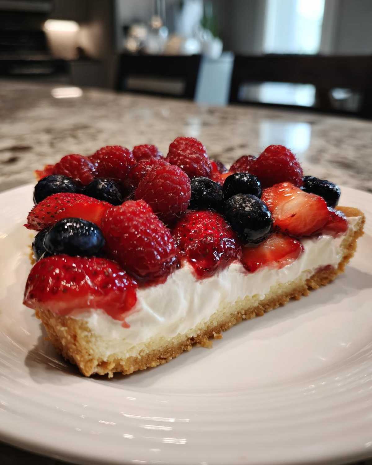 Close-up of a slice of Berry Fruit Pizza featuring a thick cream cheese layer and topped with glossy raspberries, blueberries, and strawberries.