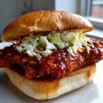 Close-up of a Spicy Gochujang Chicken Burger featuring a crispy fillet coated in red sauce and topped with coleslaw on a brioche bun.