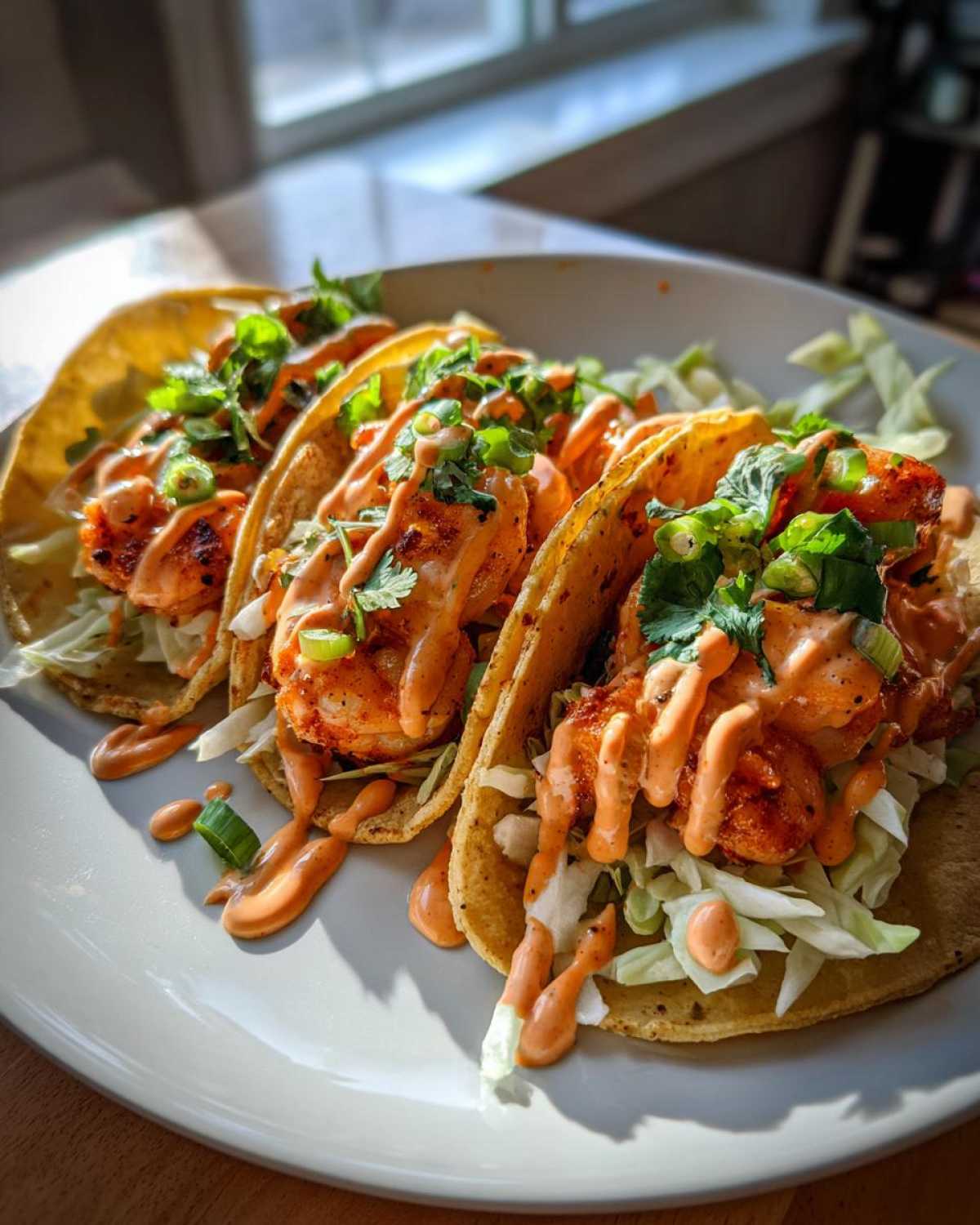 Four delicious Spicy Sriracha Mayo Shrimp Tacos filled with cabbage, shrimp, and drizzled generously with orange sauce.