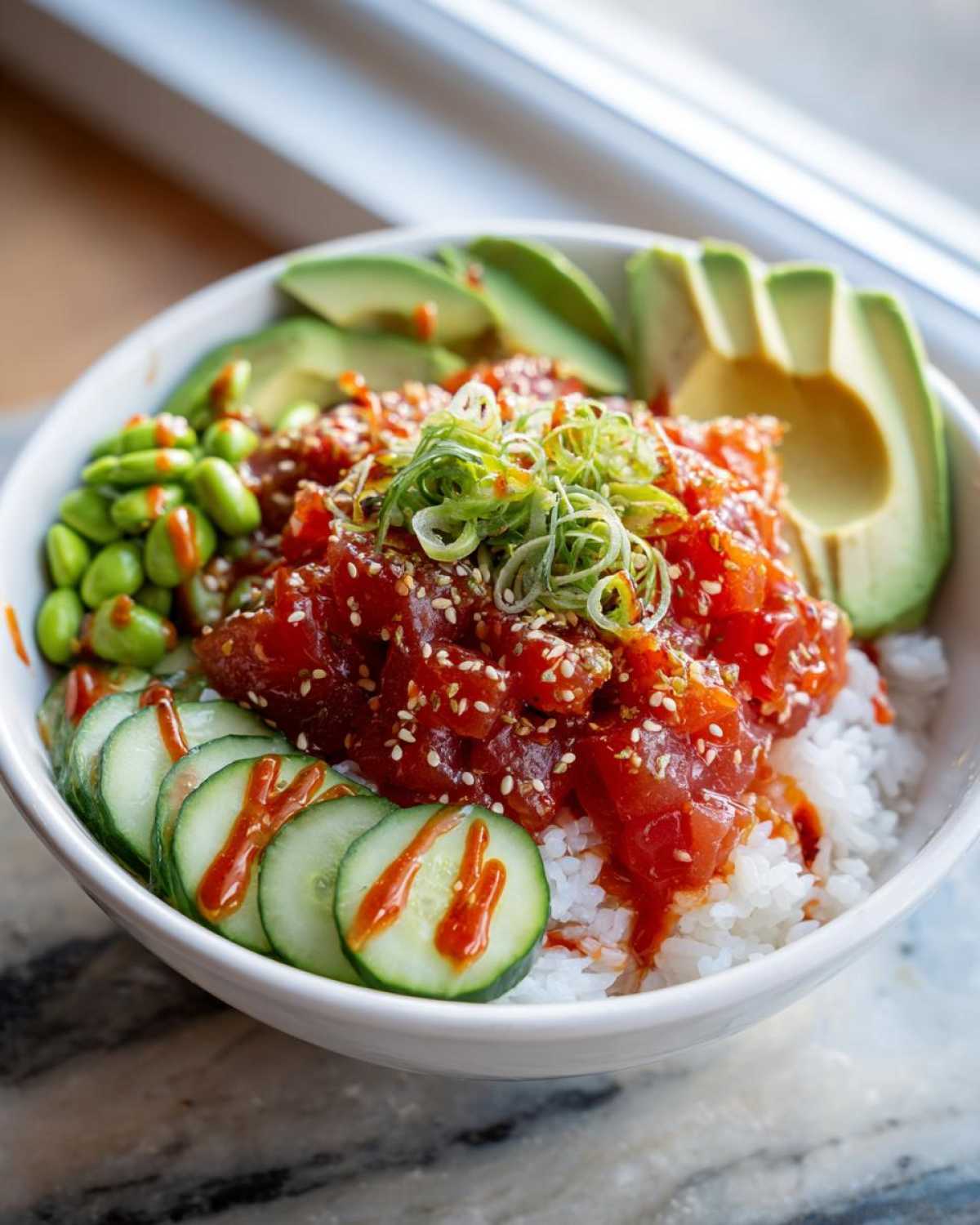 A close-up of a Spicy Tuna Bowl featuring marinated tuna over rice, topped with sesame seeds, scallions, avocado, cucumber, and edamame.