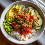 Overhead view of a delicious Spicy Tuna Bowl served over white rice with sliced avocado, edamame, and cucumber.