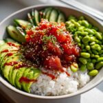 A close-up overhead view of a vibrant Spicy Tuna Bowl featuring marinated tuna over rice, sliced avocado, edamame, and cucumber.