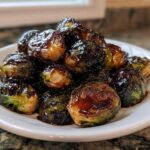 A pile of roasted Brussels sprouts generously coated in a thick, dark Sticky Brussels Sprouts Glaze on a white plate.