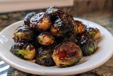 A pile of roasted Brussels sprouts generously coated in a thick, dark Sticky Brussels Sprouts Glaze on a white plate.