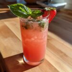 A tall glass filled with pink Strawberry Basil Lemonade, garnished with fresh basil and a strawberry slice.