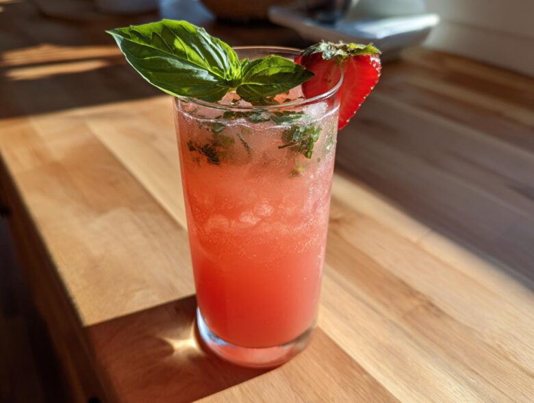 A tall glass filled with pink Strawberry Basil Lemonade, garnished with fresh basil and a strawberry slice.