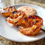 Close-up of grilled Sweet Chili Grilled Bang Bang Shrimp Skewers glazed with sauce, served with a side of creamy dipping sauce.