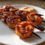 Close-up of grilled Sweet Chili Grilled Bang Bang Shrimp Skewers served on a white plate with a side of dipping sauce.