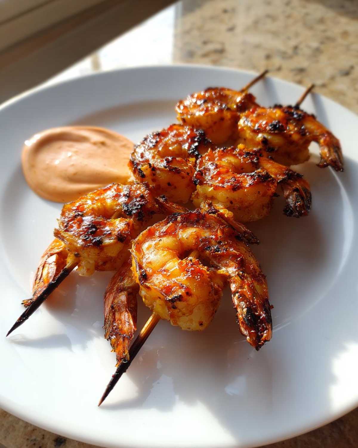 Close-up of grilled Sweet Chili Grilled Bang Bang Shrimp Skewers served with a side of creamy orange dipping sauce on a white plate.