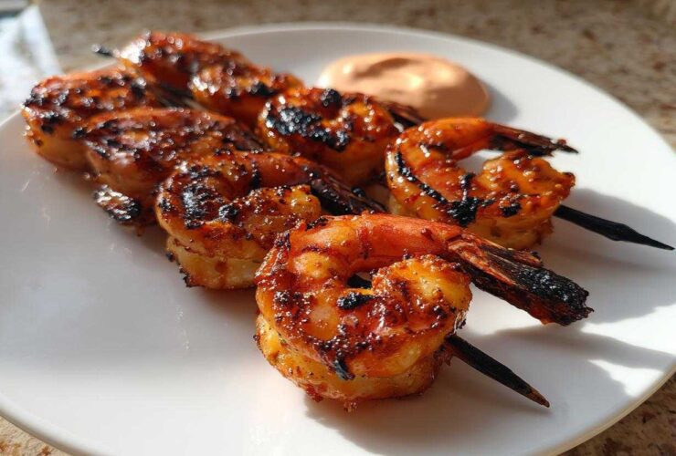 Close-up of grilled Sweet Chili Grilled Bang Bang Shrimp Skewers served on a white plate with a side of dipping sauce.