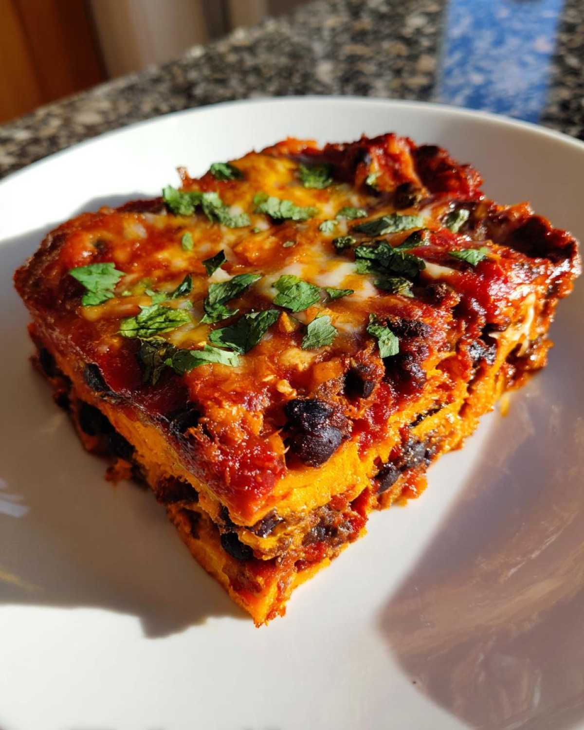 A hearty slice of Sweet Potato and Black Bean Enchilada Casserole layered with sweet potato, black beans, sauce, and melted cheese.