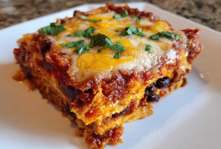 A close-up serving of Sweet Potato and Black Bean Enchilada Casserole topped with melted cheese and cilantro.