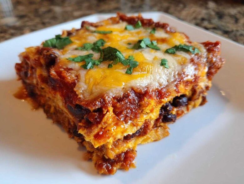 A close-up serving of Sweet Potato and Black Bean Enchilada Casserole topped with melted cheese and cilantro.