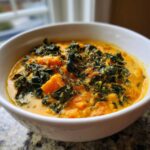 Close-up of a bowl of creamy Sweet Potato Chowder Kale, topped with dark green kale and fresh thyme sprigs.