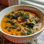 A close-up of a creamy orange Sweet Potato Chowder Kale topped with fresh thyme in a white bowl.