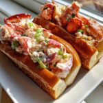 Two generously filled Lobster Rolls, showcasing creamy lobster salad and bright green scallions on toasted buns.
