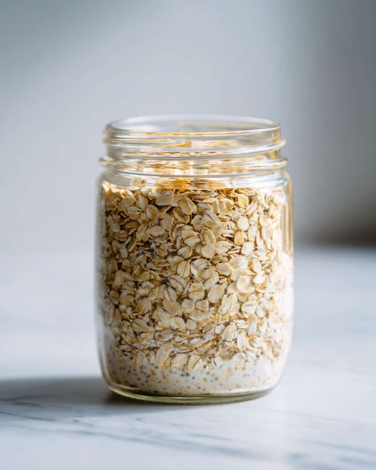 Close-up of rolled oats layered over liquid and chia seeds in a glass jar, ready for Overnight Oats.