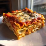 Close-up of a perfectly layered slice of Vegan Dumpling Lasagna, topped with rich tomato sauce and melted vegan cheese.