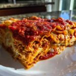 A close-up, sunlit serving of Vegan Dumpling Lasagna showing layers of pasta, rich filling, and tomato sauce.